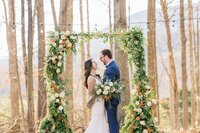 Bride and groom framed by lush greenery wedding arbor designed by Flowergirl Cville, Charlottesville florist | Photo by Xiaoqi Li Photography