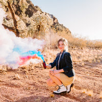high school senior girl wearing blazer holding two smoke bombs in field