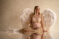Blonde pregnant woman sits in angel wings and gold gown at our Waukesha County studio.