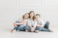 A photo of 3 young siblings sitting on the floor leaning on each other at a photography studio in Fort Worth TX.