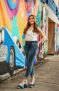 Senior portrait in downtown Mobile, Alabama — hands in back pocket standing on the sidewalk near a wall of art.
