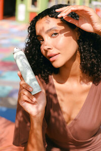 Model holding Evian Protect mist in dappled afternoon light