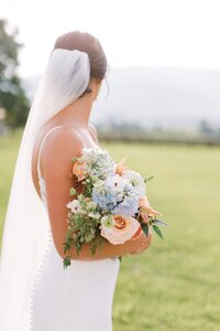 Bride holding a peach and light blue bridal bouquet with Queen Anne's Lace at King Family Vineyard in Crozet, Virginia — florals by Flowergirl Cville, Charlottesville wedding florist | Photo by Paige Ryan Photography