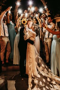 Bride and groom kissing as wedding guests cheer and hold up sunflowers