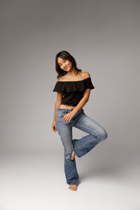 Full-length studio portrait of a high school senior girl posing in a black top and jeans, studio senior photography by Kaitlyn Dawn Photography.