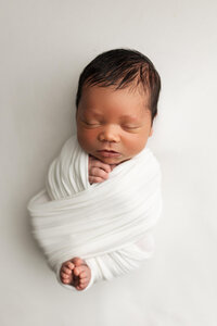 Newborn Baby boy wrapped in a white knit wrap on a white backdrop at Jennifer Brandes Photography near Mankato, MN