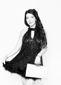 Luxury fine art portrait from Luxe Portraiture LV featuring a woman in a sleeveless sequined black dress with feathered hemline, keyhole neckline, clutch bag, and decorative headpiece, captured in timeless black‑and‑white portrait photography that highlights vintage glamour and sophistication.