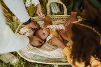 Newborn boy in a moses basket with his entire family laying their hands on him