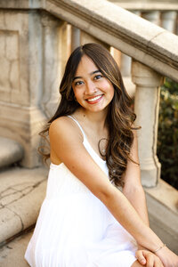 High school senior girl in a white dress sitting on stone steps, natural light senior portrait by Kaitlyn Dawn Photography.