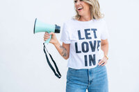 A woman life coach holding a megaphone with a tshirt on that says Let Love In to promote her podcast.
