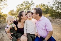 A mom and dad kiss their young son as he smiles