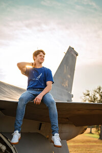 Senior portrait at Battleship Memorial Park in Mobile, Alabama— holding his neck and sitting on the wing of an airplane.