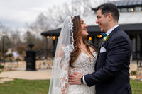 A wedding couple with their arms around each other smiling at each other