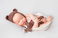 Sleeping newborn baby wearing knit bear bonnet and wrapped in cream fabric