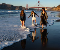 a mother with her two daughters walking down the beach at sunset as the surf comes in with the golden gate bridge in the background