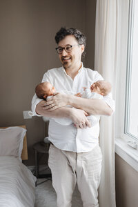 new dad holding his twin daughters captured by Toronto Newborn Photographer Claire Binks