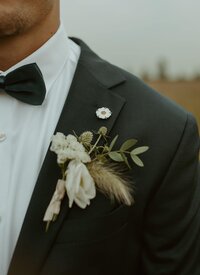 A closeup of a groom's boutonniere with soft white florals and sage greenery
