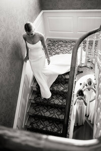 A refined composition of a bride descending a staircase to meet her bridesmaids, capturing a genuine connection and real moment.