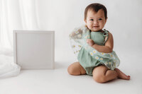 Charleston Cake Smash Photographer - Baby smiles at the camera during Milestone Portrait Session at Holy City Babies in Charleston, SC.