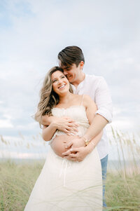 Couple laughing and holding belly together in Key Biscayne grass, maternity photos Miami