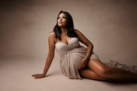 Pregnant woman with dark hair sitting on the floor in beige dress photo taken by Detroit maternity photographer Kat Figlak