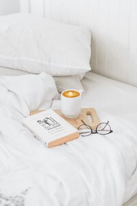 Notebook and coffee and glasses on a cozy white bed