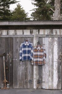 Two plaid flannel overshirts hung on a weathered boathouse door