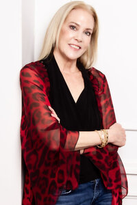 Personal branding headshot Three Stories Jewelry Co Owner Barbara Laird standing against pale wall arms crossed while smiling wearing red and black print blouse