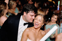 The groom leans in to whisper something to the bride, making her laugh joyfully during the wedding reception.
