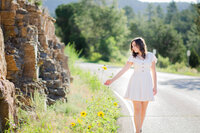 senior girl walking on the side of a road and reaching out to touch some sunflowers.