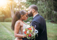 Groom kissing brides forehead while she holds a colorful bouquet of flowers