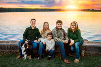 Family seated together by the water at sunset during a New Bern family photo session