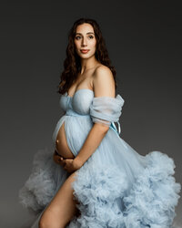 Pregnant woman in a soft blue tulle gown gently holding her belly during a maternity session with Kaitlyn Dawn Photography in Yucaipa.