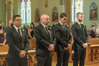 Groomsmen praying during the wedding ceremony in a Los Angeles church, captured in a candid documentary style.