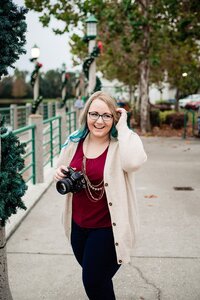 Mahlia wearing a red shirt and rose gold sweater holding a Nikon camera