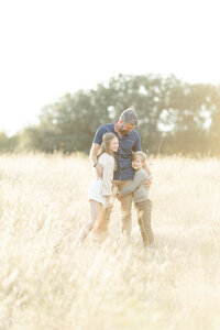 Dad holding his two children close as they stand together in the middle of a grassy field at a Fort Worth park.