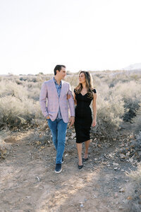 Couple from the Parker family walking together through a sunlit desert landscape in Las Vegas, sharing a romantic moment during a natural light family photography session.