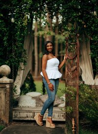Senior portrait at Bella Sera Gardens in Loxley, Alabama — holding an old metal garden gate
beneath an arch of jasmine greenery.