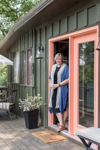 A woman in a blue sweater and black dress standing in the orange doorframe of a house at Hillside  Hideaway