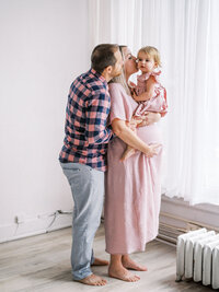 Family shot of a mom kissing her daughter while her husband hugs them.