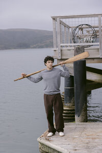 Grey crewneck and brown trousers carrying an oar along the dock