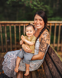 Mother holding her baby on a wooden dock surrounded by trees during a family photography session in Eastern North Carolina