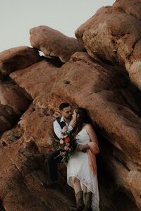 Couple embracing on red rock formations holding a bouquet