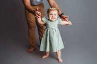 Charleston Baby Milestone Photographer - Father holds his baby's hands to help her walk during her Milestone Portrait Session at Holy City Babies Portrait Studio in Charleston, SC.