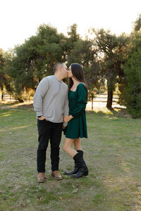Couple standing close together in a sunlit park surrounded by trees, romantic outdoor portrait by Kaitlyn Dawn Photography, natural light family photographer.