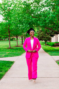 Lipscomb senior walking down side walk smiling while wearing cap and a hot pink power suit