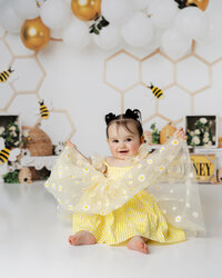 Adorable little one glowing in her sunshine yellow dress, ready to buzz into her cake smash session! Captured by Yucaipa cake smash photographer Kaitlyn Dawn Photography.