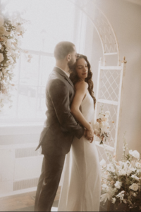 Groom kissing bride under floral arch at Maison Charlottesville. Florals by Flowergirl Cville and photo by Amy Mitchell Photography