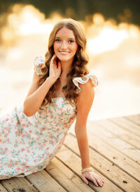Senior portrait in downtown Magnolia Springs, Alabama — touching her face in a flowery dress.