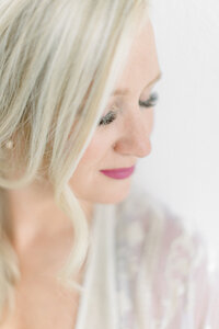 Close up light filled boudoir portrait of a woman wearing a lace robe as she looks to her side as her hair falls on her face.